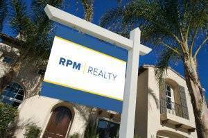 RPM Realty sign hanging in a front yard next to palm trees